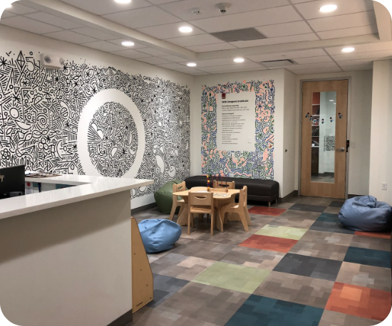 A view of a lobby with a intricate black and white doodle mural on the wall, two bean bags, and a small wooden table and chairs.